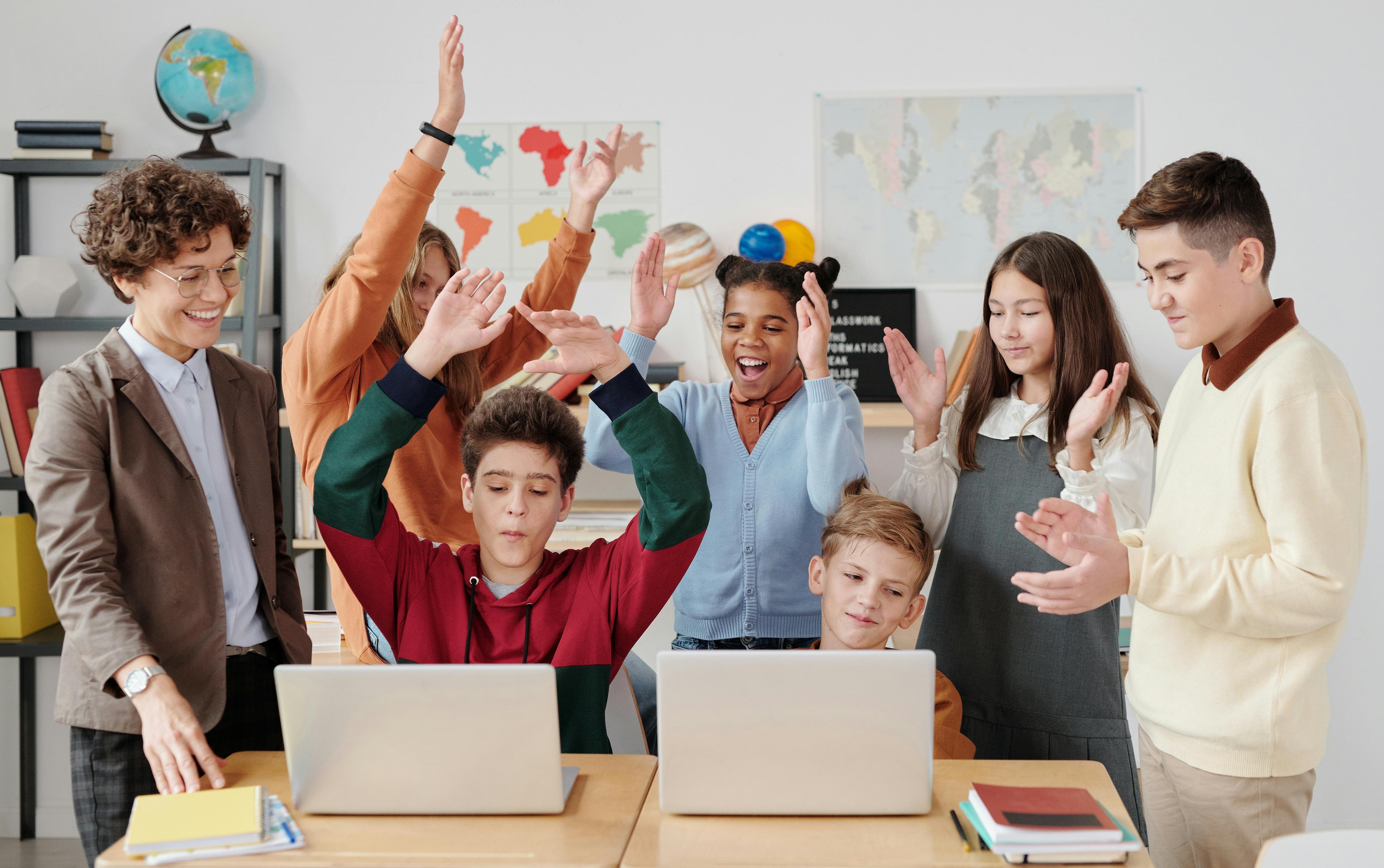 Smiling school students and teacher interacting with laptops in a classroom